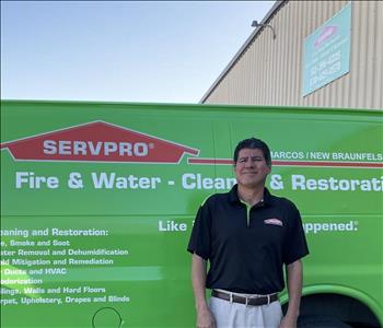 Male Employee of SERVPRO wearing a black short sleeve collared shirt standing in front of green SERVPRO van