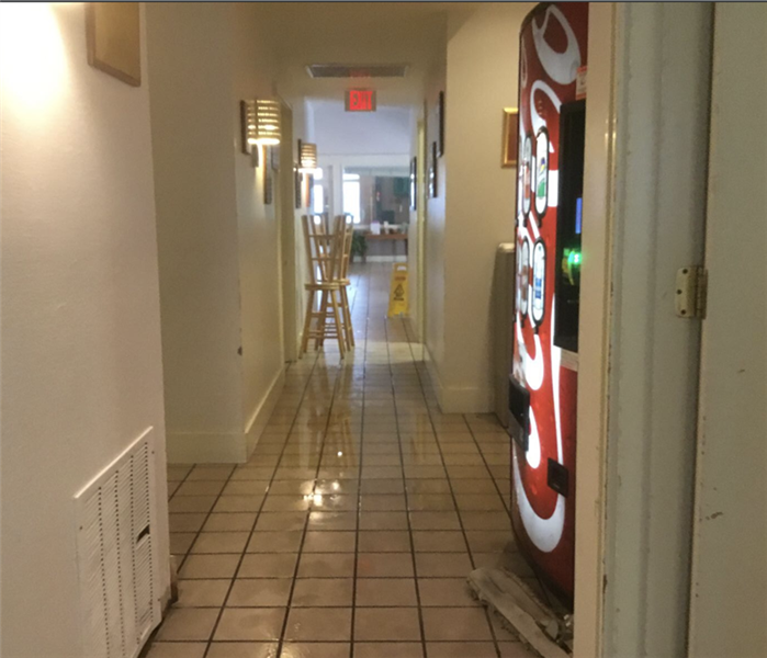 Hallway with standing water on the floor. There is a coke machine in the hall as well as two lone bar stools