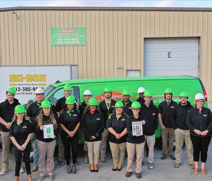 The employees from SERVPRO of San Marcos/New Braunfels gather outside in front of company vehicles holding two magazines